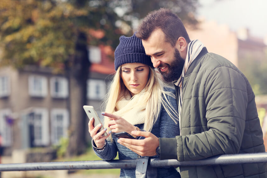 couple interacting over a cell phone on a bridge. 