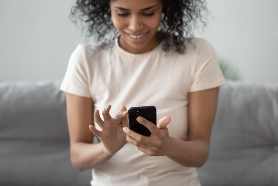 pretty coloured girl sitting on the sofa smiling and using her cellphone. 