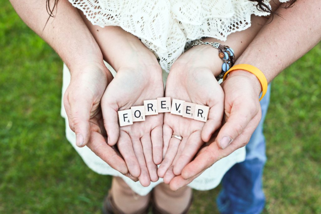 couple holding hands and forming the the word 'forever' with scrabble pieces.