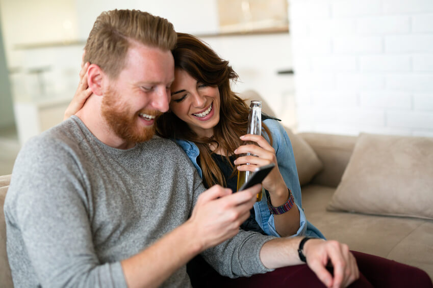 Good looking couple chilling in  the living room and using smart phone together