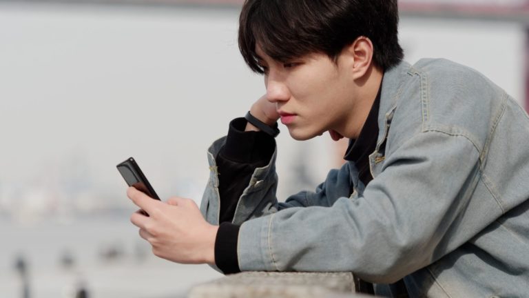 handsome asian single guy looks at his phone discouraged
