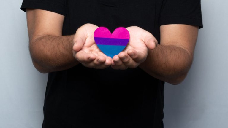 man holds paper heart with bisexuality pride colors in his hands