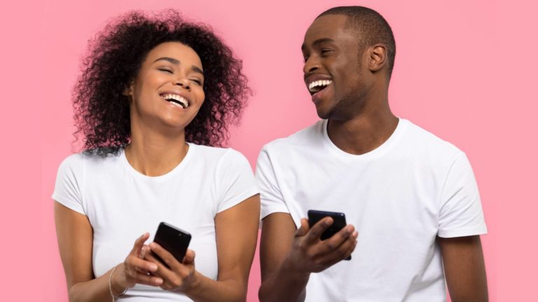 man and woman in relationship laugh while using their smartphones