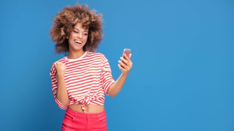 woman with afro hairstyle is cheering while holding her phone