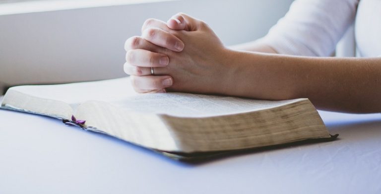 Woman praying with hands atop a bible