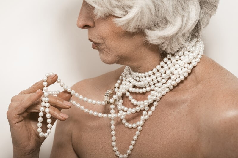 naked senior woman playing with her pearl necklace