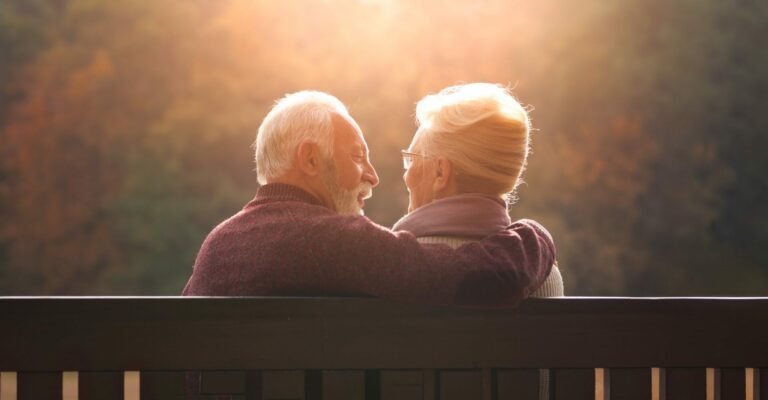 senior couple sitting on a bench in the sunset